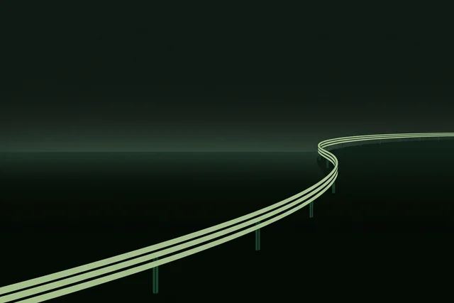 A single lit guardrail curving away into the dark, holding the line of a road that is otherwise empty.